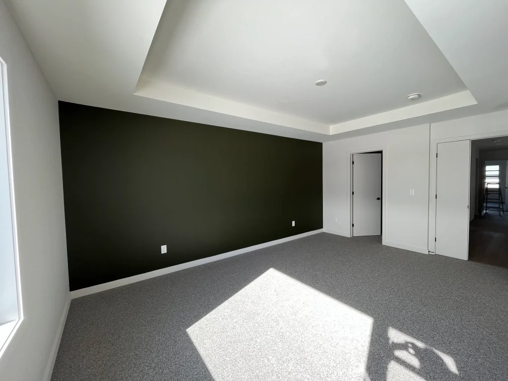 Spacious modern bedroom featuring a bold dark charcoal black accent wall, bright white tray ceiling structure, smooth off-white surrounding walls, and clean baseboard trim in an Ottawa home.