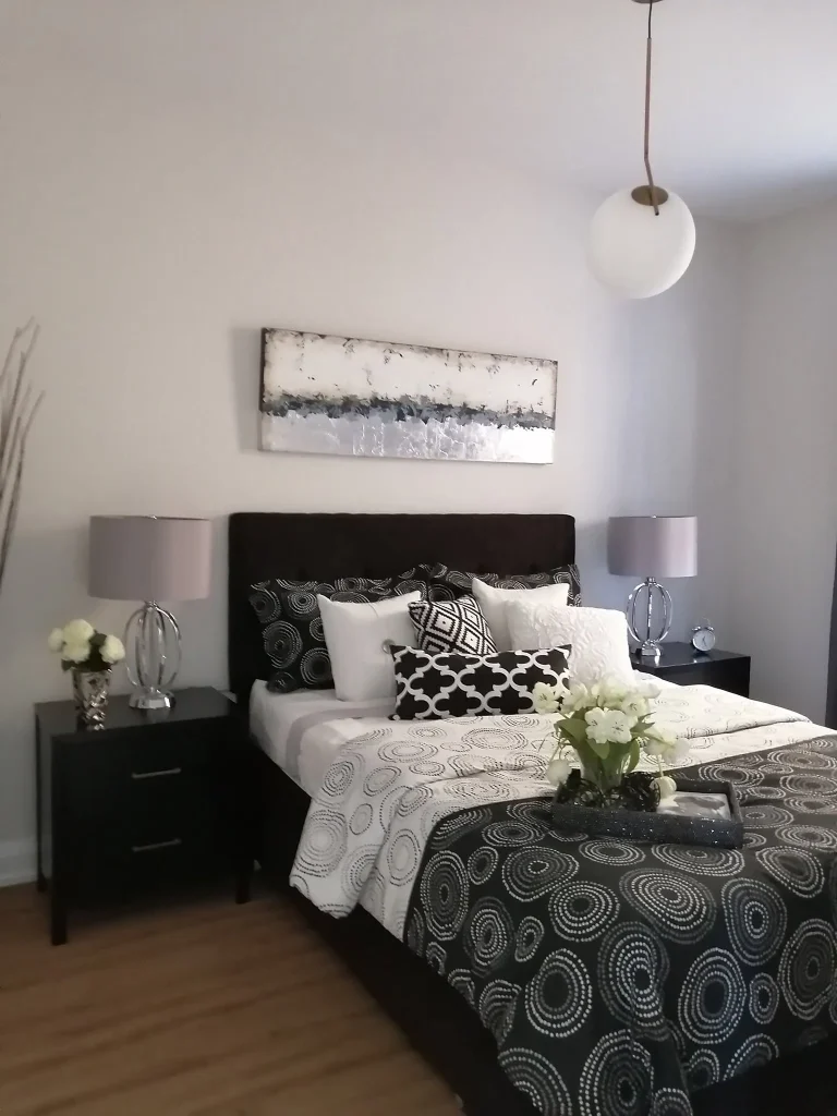 Elegantly styled primary bedroom in an Ottawa home featuring soft greige painted walls, smooth white ceiling, black upholstered headboard, and clean baseboard trim work.