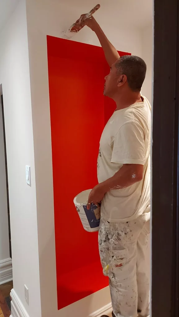 Professional Ottawa painter cutting in crisp white paint lines along a bold vibrant red accent wall niche using a hand sash brush and cut bucket.