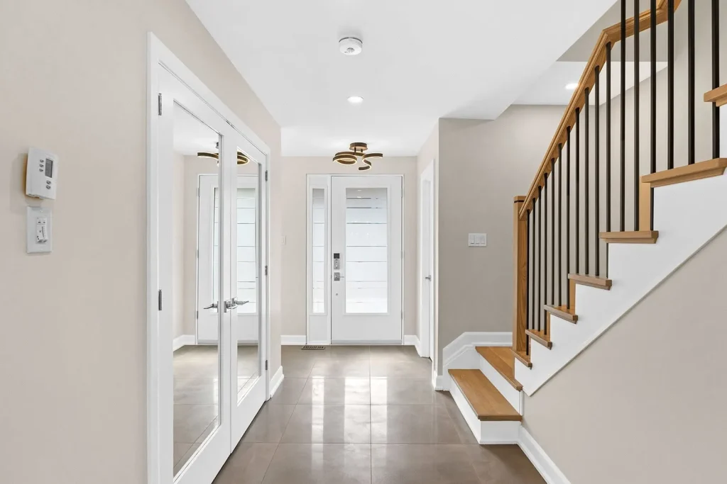 Modern home main entrance foyer featuring smooth off-white painted walls, bright white interior doors and baseboards, smooth flat ceiling, and wood-and-iron staircase trim in Ottawa.