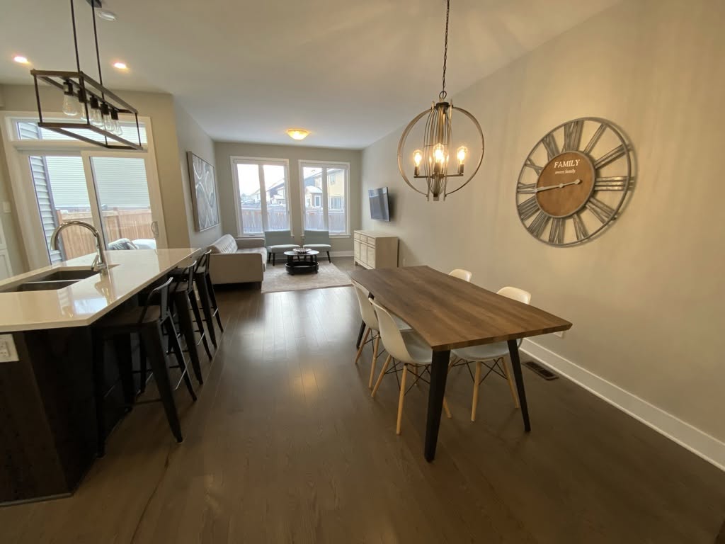 Open-concept Ottawa home living room and dining area featuring warm taupe painted walls, white ceiling and baseboard trim, dark wood flooring, and modern lighting fixtures.